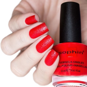 Pode incluir: Um frasco de esmalte de unha vermelho com tampa preta e o nome da marca "Sophin" impresso no rótulo. O rótulo também inclui o texto "Vernis à ongles Nail Polish - Nagellak" e "12 ml e 0.41 fl.oz".