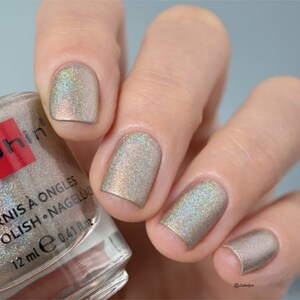 May include: A clear glass bottle of nail polish with a silver cap. The bottle is labeled "Vernis &agrave; Ongles Polish - Nagellac" and "12 ml e 0.41 fl oz". The bottle is sitting on a hand with four fingers painted with a shimmery silver nail polish.