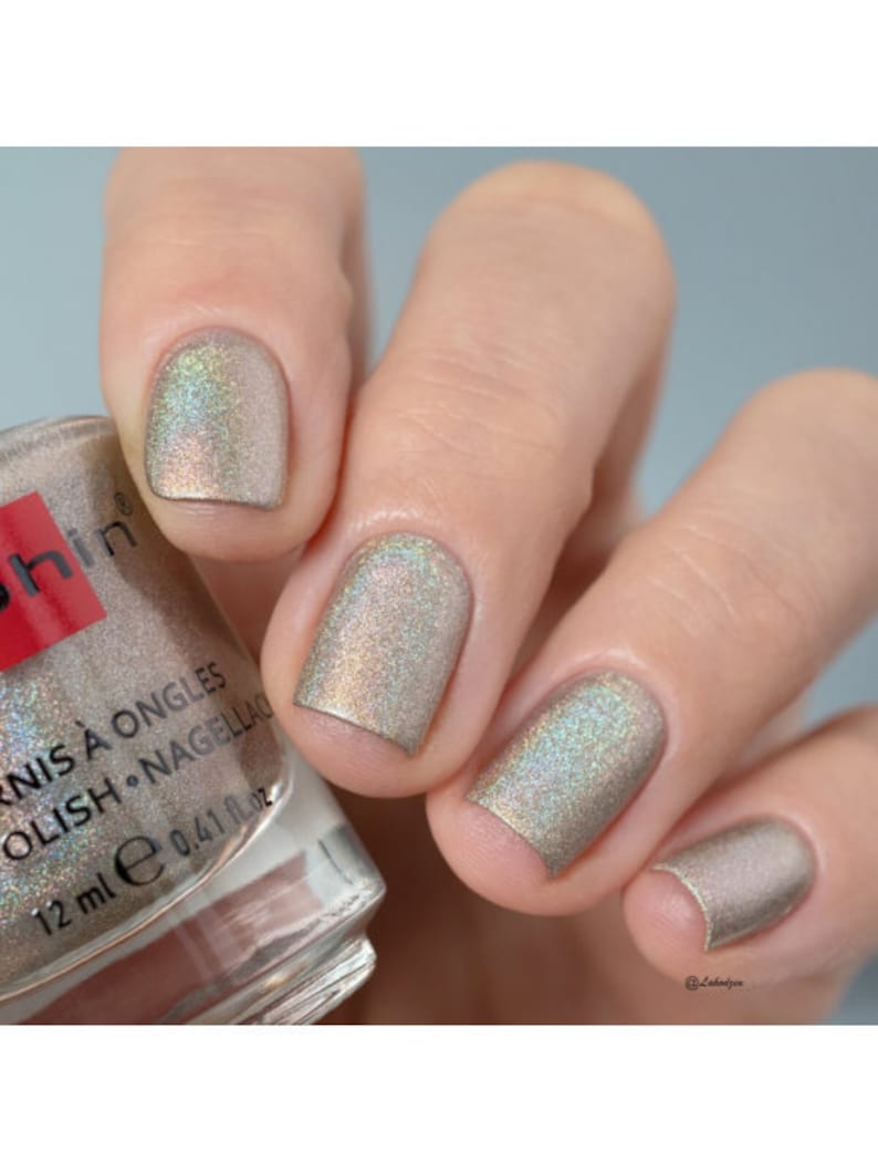 May include: A clear glass bottle of nail polish with a silver cap. The bottle is labeled "Vernis &agrave; Ongles Polish - Nagellac" and "12 ml e 0.41 fl oz". The bottle is sitting on a hand with four fingers painted with a shimmery silver nail polish.