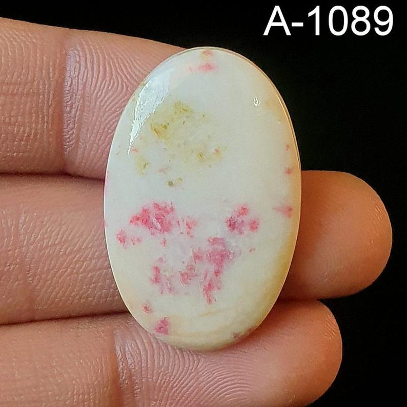 May include: Oval shaped cabochon gemstone with a white base and pink and yellow inclusions. The stone is approximately 1 inch in diameter.
