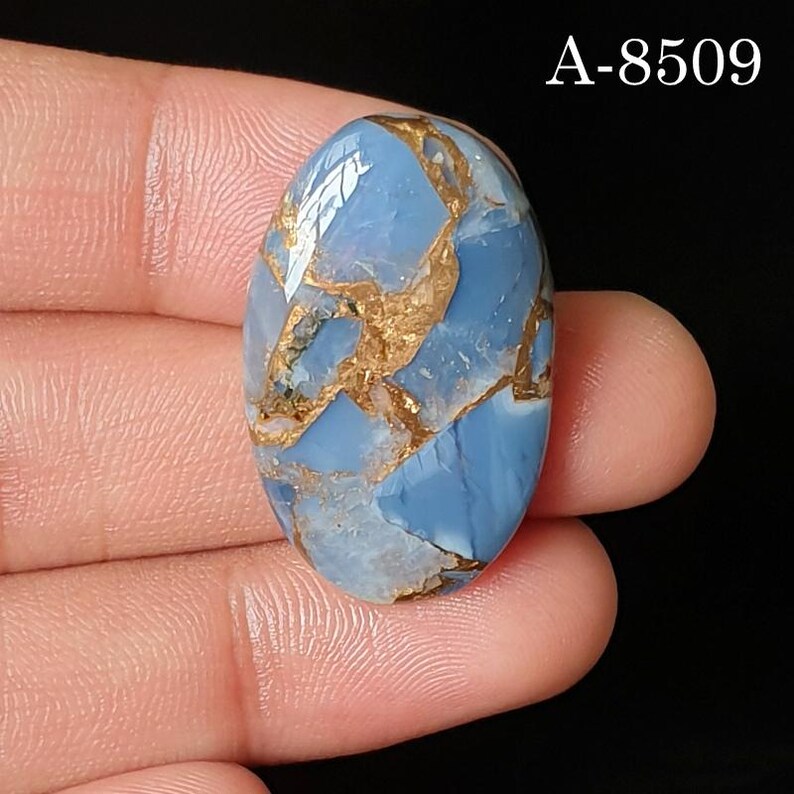 May include: An oval-shaped blue gemstone with a smooth, polished surface featuring intricate, branching copper-colored veins throughout. The stone displays a glossy finish and is marked with the text A-8509 in the upper right corner.