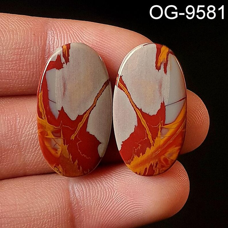 May include: Pair of oval-shaped cabochon gemstones with a red, white, and yellow marbled pattern. The stones are approximately 1 inch in length.