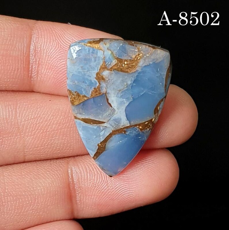 May include: A triangular-shaped blue gemstone with a smooth, polished surface featuring intricate copper-colored veining throughout. The stone displays a mix of light and medium blue tones. The text A-8502 is visible in the upper right corner.