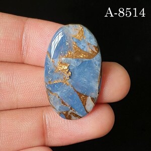 May include: An oval-shaped cabochon gemstone featuring a light blue base with intricate, jagged copper-colored metallic veining throughout the surface. The stone displays a smooth, polished finish and includes the text A-8514 in the upper right corner.