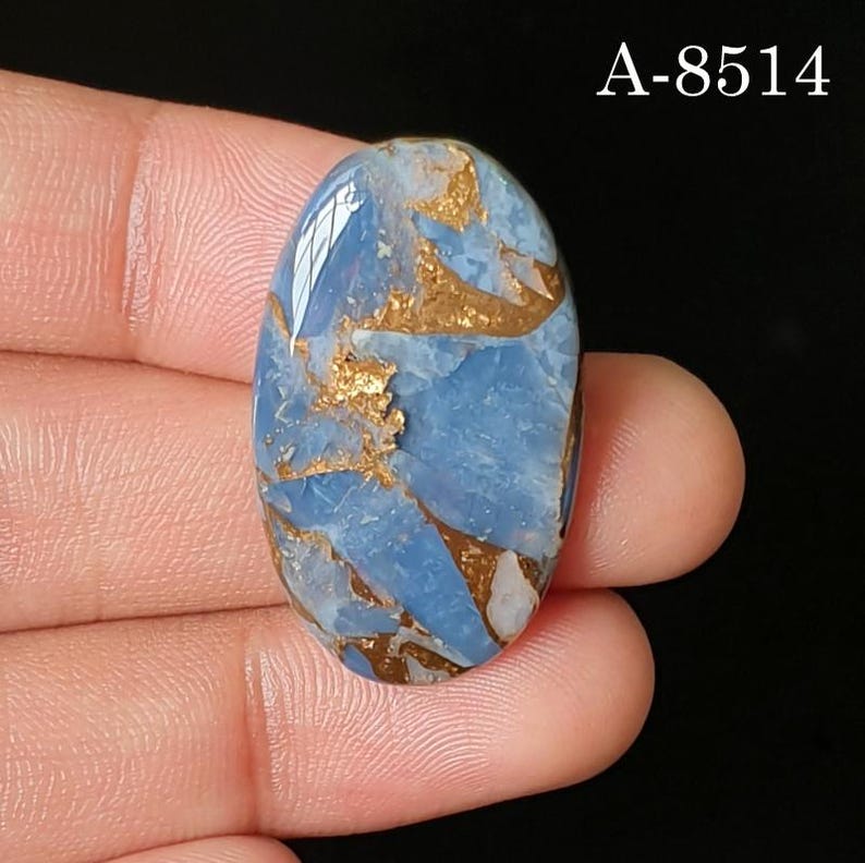 May include: An oval-shaped cabochon gemstone featuring a light blue base with intricate, jagged copper-colored metallic veining throughout the surface. The stone displays a smooth, polished finish and includes the text A-8514 in the upper right corner.