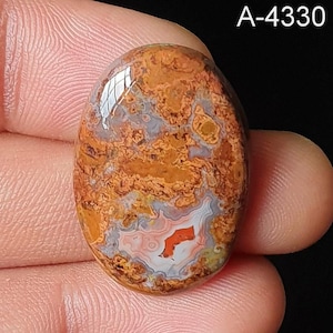 Puede incluir: Gema ovalada con superficie pulida. La piedra presenta una mezcla de patrones naranjas, marrones, grises y blancos, con un diseño central rojo y blanco. El texto "A-4330" es visible en la esquina superior derecha.