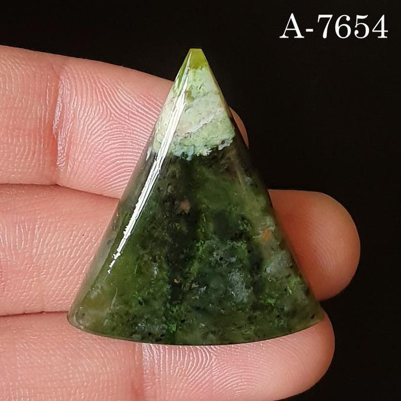 May include: A triangular gemstone with a polished surface. The stone features a gradient of green hues, with a lighter, almost white, section at the apex. The text "A-7654" is visible in the upper right corner.