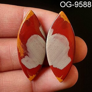 May include: Two red, white, and orange agate cabochons with a teardrop shape. The cabochons have a polished finish and are set in a pair of earrings. OG-9588