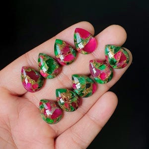 May include: A collection of nine teardrop-shaped cabochons featuring a vibrant mosaic pattern of bright pink and emerald green segments interspersed with metallic copper-colored veins, all polished to a smooth, reflective finish.