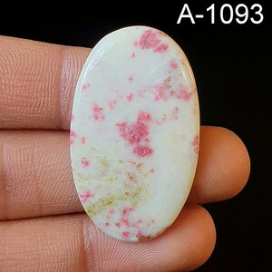 May include: A white oval cabochon with pink and gold flecks. The stone is approximately 2 inches long and 1 inch wide. A-1093