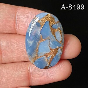 May include: An oval-shaped blue gemstone with a polished surface featuring intricate copper-colored veining throughout the stone. The text A-8499 is clearly visible in the upper right corner of the image, set against a dark background.