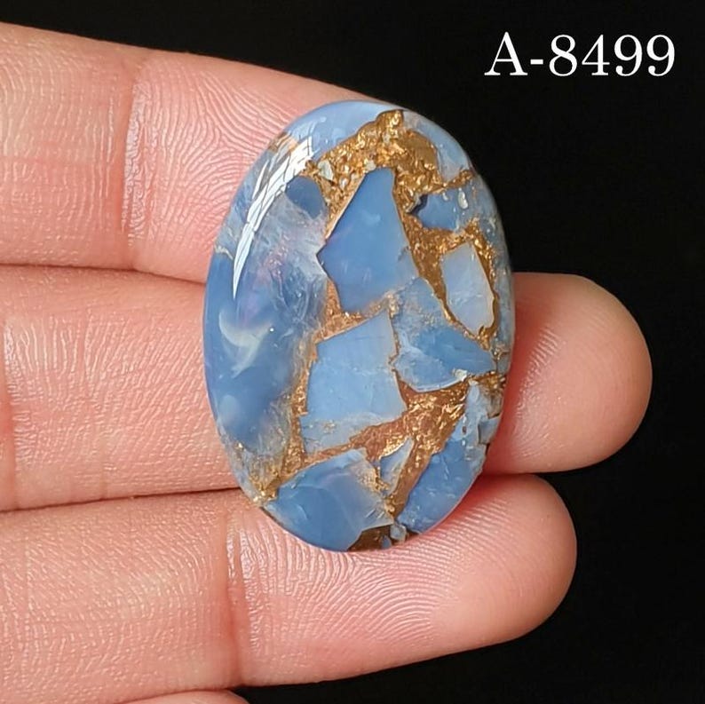 May include: An oval-shaped blue gemstone with a polished surface featuring intricate copper-colored veining throughout the stone. The text A-8499 is clearly visible in the upper right corner of the image, set against a dark background.