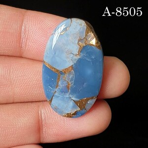 May include: An oval-shaped blue gemstone with a smooth, polished surface featuring intricate copper-colored veining throughout the stone. The text A-8505 is visible in the upper right corner of the image against a dark background.