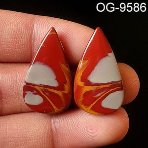 May include: Two teardrop-shaped red, white, and yellow jasper cabochons. The cabochons have a swirling pattern of red, white, and yellow.