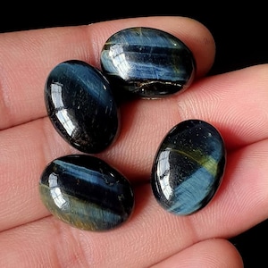 May include: Four polished, oval-shaped gemstones. The stones display a mix of deep blue and golden-yellow hues, with a glossy, reflective surface. The gemstones are smooth and appear to be natural, with unique patterns and color variations.