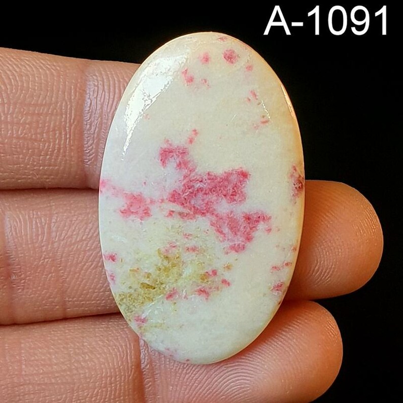 May include: Oval shaped cabochon gemstone with a white base and pink and gold inclusions. The stone is approximately 2 inches long. A-1091