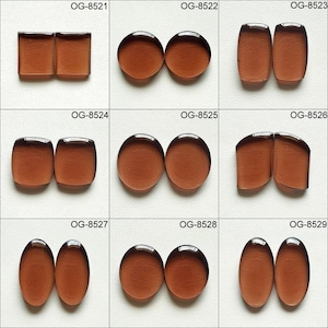 May include: Nine pairs of glass cabochons in various shapes and sizes. The cabochons are all a deep brown colour and have a slightly textured surface.
