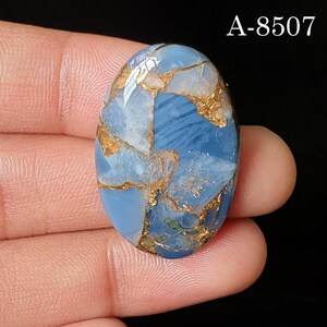 May include: An oval-shaped blue gemstone cabochon featuring intricate copper-colored veining throughout the surface. The stone displays a polished, smooth finish with varying shades of light and dark blue. The text A-8507 is visible in the corner.