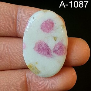 May include: White oval cabochon with pink and gold inclusions. The stone is approximately 2.5 cm long and 1.5 cm wide. A-1087