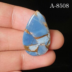 May include: A teardrop-shaped blue gemstone with a smooth, polished surface featuring intricate copper-colored veining throughout the stone. The text A-8508 is visible in the upper right corner of the image, set against a dark background.