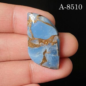 May include: A polished, semi-oval shaped blue gemstone featuring intricate, jagged copper-colored matrix veins throughout its surface. The stone displays a smooth, glossy finish with a distinct light blue hue. The text A-8510 is visible in the corner.