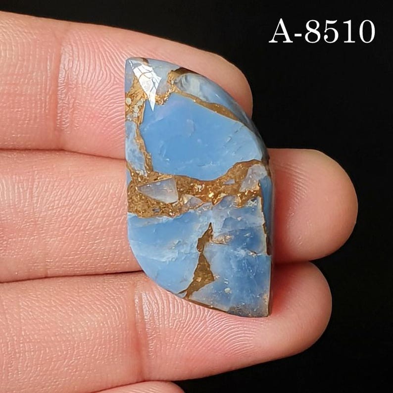 May include: A polished, semi-oval shaped blue gemstone featuring intricate, jagged copper-colored matrix veins throughout its surface. The stone displays a smooth, glossy finish with a distinct light blue hue. The text A-8510 is visible in the corner.