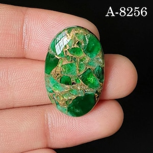 Pode incluir: Uma pedra preciosa oval de cor verde com uma superfície polida apresentando veios dourados intrincados. A pedra exibe um tom esmeralda vibrante com reflexos brilhantes e está marcada com o texto A-8256 no canto superior direito.