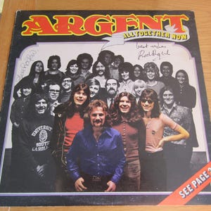Pode incluir: Capa do álbum "All Together Now" de Argent. A capa apresenta uma foto em grupo dos membros da banda e o título do álbum em letras grandes e em negrito. A capa tem uma estética vintage, com uma faixa vermelha que diz "Ver página 2".