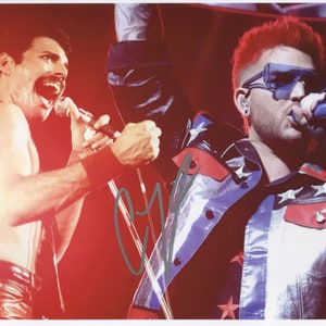 May include: A black and white photograph of two singers performing on stage. The singer on the left is wearing a black leather jacket and a black leather belt. The singer on the right is wearing a blue and red jacket with white stars. Both singers are holding microphones.