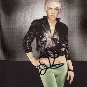 Könnte beinhalten: Eine Frau mit kurzen, platinblonden Haaren trägt eine schwarze Lederjacke und eine grüne Hose. Sie steht vor einem schwarz-weißen Gitterhintergrund.