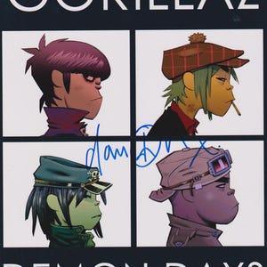 Könnte beinhalten: Ein Gorillaz Demon Days Albumcover-Druck mit vier illustrierten Charakterporträts in einem Raster. Der obere Text lautet GORILLAZ und der untere Text DEMON DAYS. Eine blaue Tintensignatur ist in der Mitte des Bildes zu sehen.