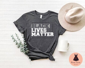 May include: A dark gray t-shirt with the text "BLACK LIVES MATTER" printed in white on the front. The text is in a bold, blocky font and is surrounded by a black rectangle.
