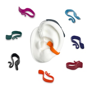Puede incluir: Una variedad de clips coloridos para audífonos en morado, verde, azul, rojo, naranja y negro. Los clips están diseñados para asegurar los audífonos, con un modelo de oreja blanca en el centro. Los clips son de material flexible.