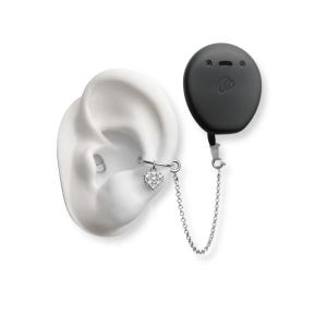 Puede incluir: Un modelo de oreja blanco con un ear cuff plateado con un dije en forma de corazón. Un dispositivo negro de forma ovalada con una cara de dibujos animados está conectado al cuff por una cadena plateada. La imagen está sobre un fondo blanco.