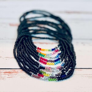 May include: A stack of black beaded necklaces with a rainbow of colored beads at the bottom.