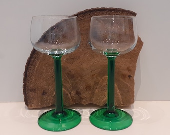 May include: Two clear glass wine glasses with green stems and bases. The glasses are sitting on a piece of wood.