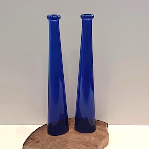 Op de afbeelding: Twee kobaltblauwe glazen vazen met een taps toelopend ontwerp, staand op een houten oppervlak.