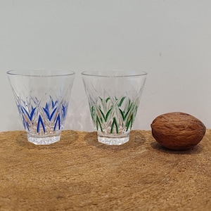 Puede incluir: Dos vasos transparentes con diseños de hojas azules y verdes. Una nuez marrón está junto a los vasos sobre una superficie de madera. Los vasos tienen un patrón decorativo.