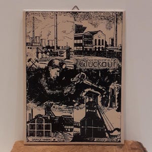 May include: A rectangular, black and white print featuring industrial scenes and a miner with the word "Glückauf". The print is divided into sections with the text "Oranje Nassau" at the top and bottom. The print is mounted on a light-colored surface.