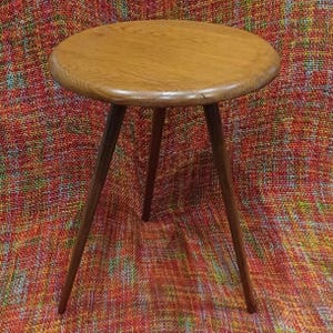 Könnte beinhalten: Kleiner, runder Beistelltisch aus Holz mit drei angewinkelten Beinen. Die Tischplatte ist hellbraun und die Beine sind dunkler braun. Der Tisch hat einen Durchmesser von ca. 46 cm und ist 51 cm hoch.