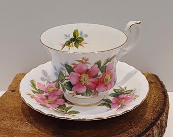 Puede incluir: Un juego de taza y platillo de té blanco con un diseño floral con rosas rosadas y hojas verdes. El juego tiene un borde dorado.