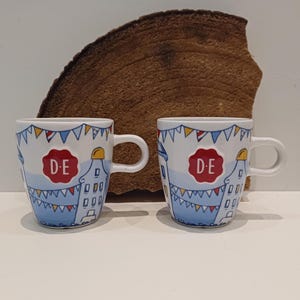 Douwe Egberts, en mugg eller set med två eller fyra muggar, bild av kanalhus, inklusive en klockgavel, relief av Douwe Egberts sigill
