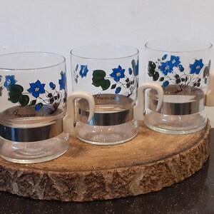 Set di tre bicchieri da tè flowerpower; con immagine di 'Anemone hepatica' in fiore blu e un manico attaccato con fascia metallica, anni '70