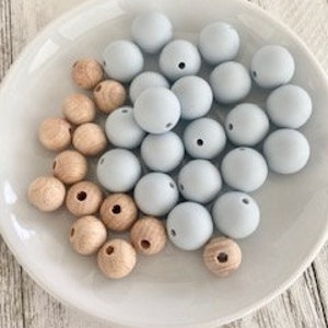 Pode incluir: Uma tigela de contas redondas de madeira natural e azul claro. As contas t&ecirc;m um furo no centro.