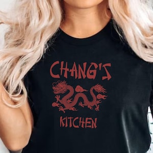 Może przedstawiać: Czarny T-shirt z czerwonym smokiem i nadrukiem "Chang's Kitchen" z przodu.
