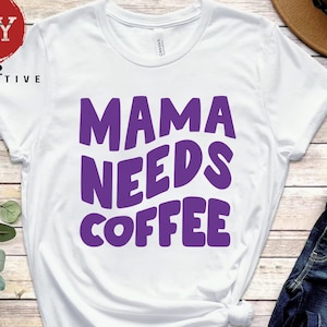 May include: White t-shirt with the text "Mama Needs Coffee" in purple letters. The letters are in a retro, rounded font.