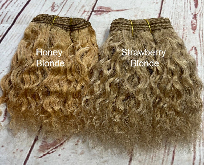 May include: Two bundles of wavy human hair extensions, one labeled "Honey Blonde" and the other labeled "Strawberry Blonde".