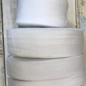 May include: A stack of four white elastic bands, each about 1 inch wide. The bands are made of a soft, stretchy material and are perfect for sewing projects.