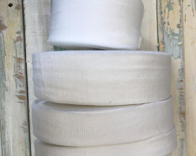 May include: A stack of four white elastic bands, each about 1 inch wide. The bands are made of a soft, stretchy material and are perfect for sewing projects.
