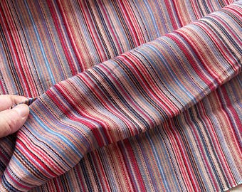 Puede incluir: Tela de rayas multicolores con una variedad de colores que incluyen rojo, azul, rosa y marrón. La tela está doblada por la mitad y las rayas son verticales.